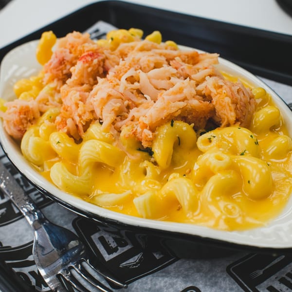 Creamy macaroni and cheese topped with a generous serving of shredded crab meat in a white bowl.
