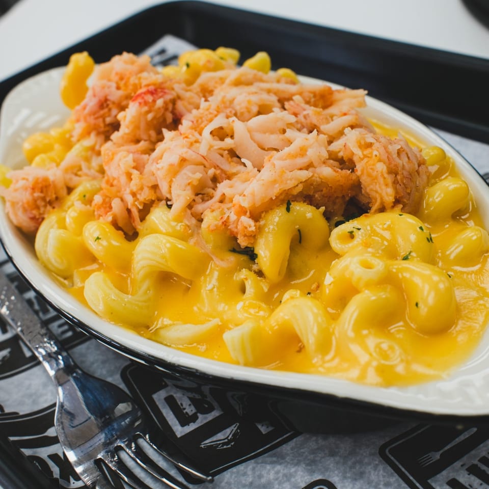 Creamy macaroni and cheese topped with a generous serving of shredded crab meat in a white bowl.