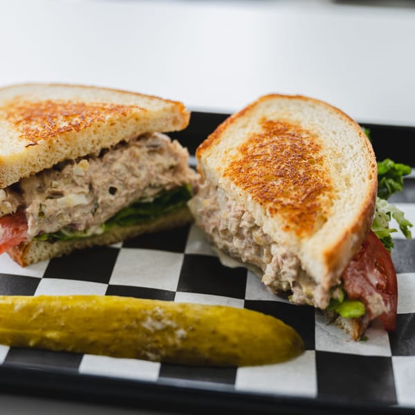 Tuna melt sandwich on toasted bread with lettuce and tomato, served with a pickle spear.