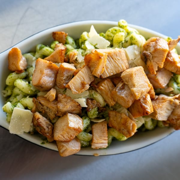 Pesto pasta with grilled chicken and parmesan cheese in a white bowl from The Lunch Box Deli.