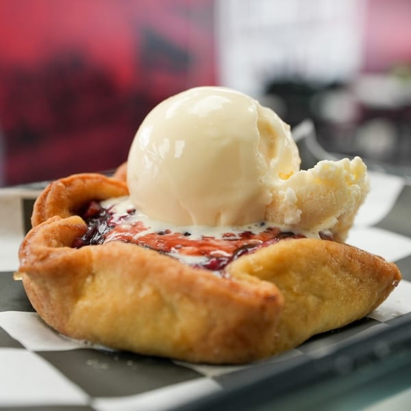 A warm fruit tart with a scoop of melting vanilla ice cream on a checkered paper.